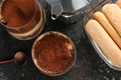 Photo of Delicious tiramisu in glasses and ingredients on grey textured table, flat lay