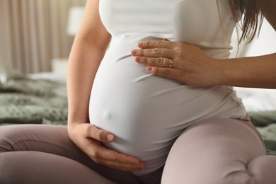 Young pregnant woman sitting on bed indoors, closeup