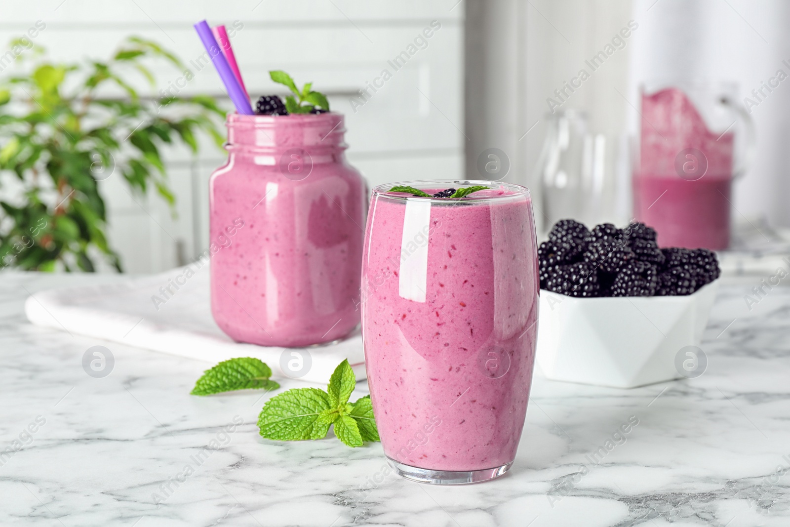 Photo of Glass and mason jar of tasty blackberry smoothie on white marble table