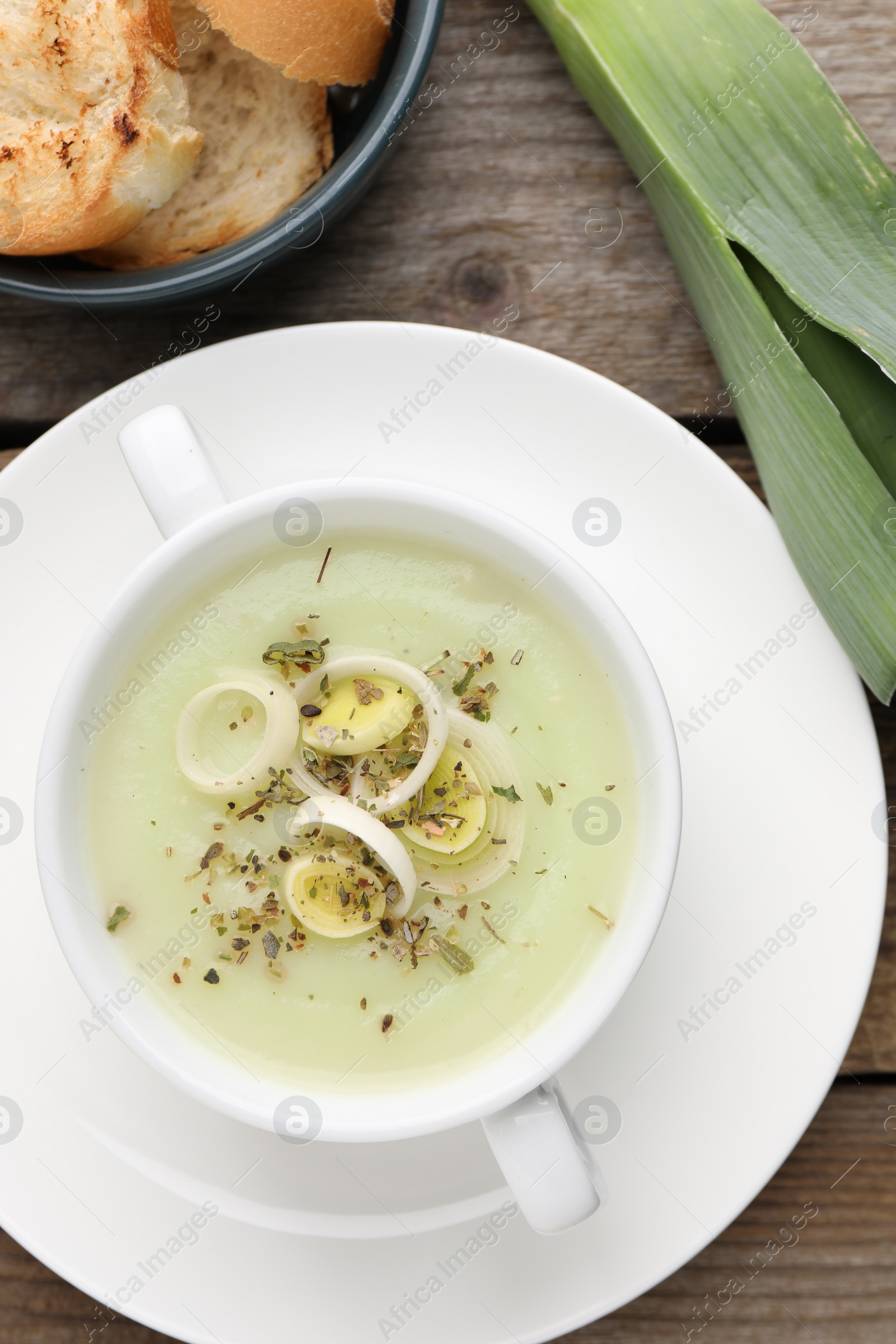 Photo of Delicious cream soup with leek and spices in bowl on wooden table, flat lay