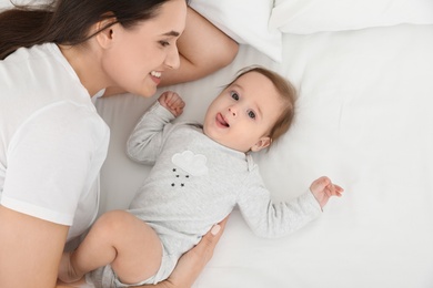 Cute baby with mother lying on bed, above view