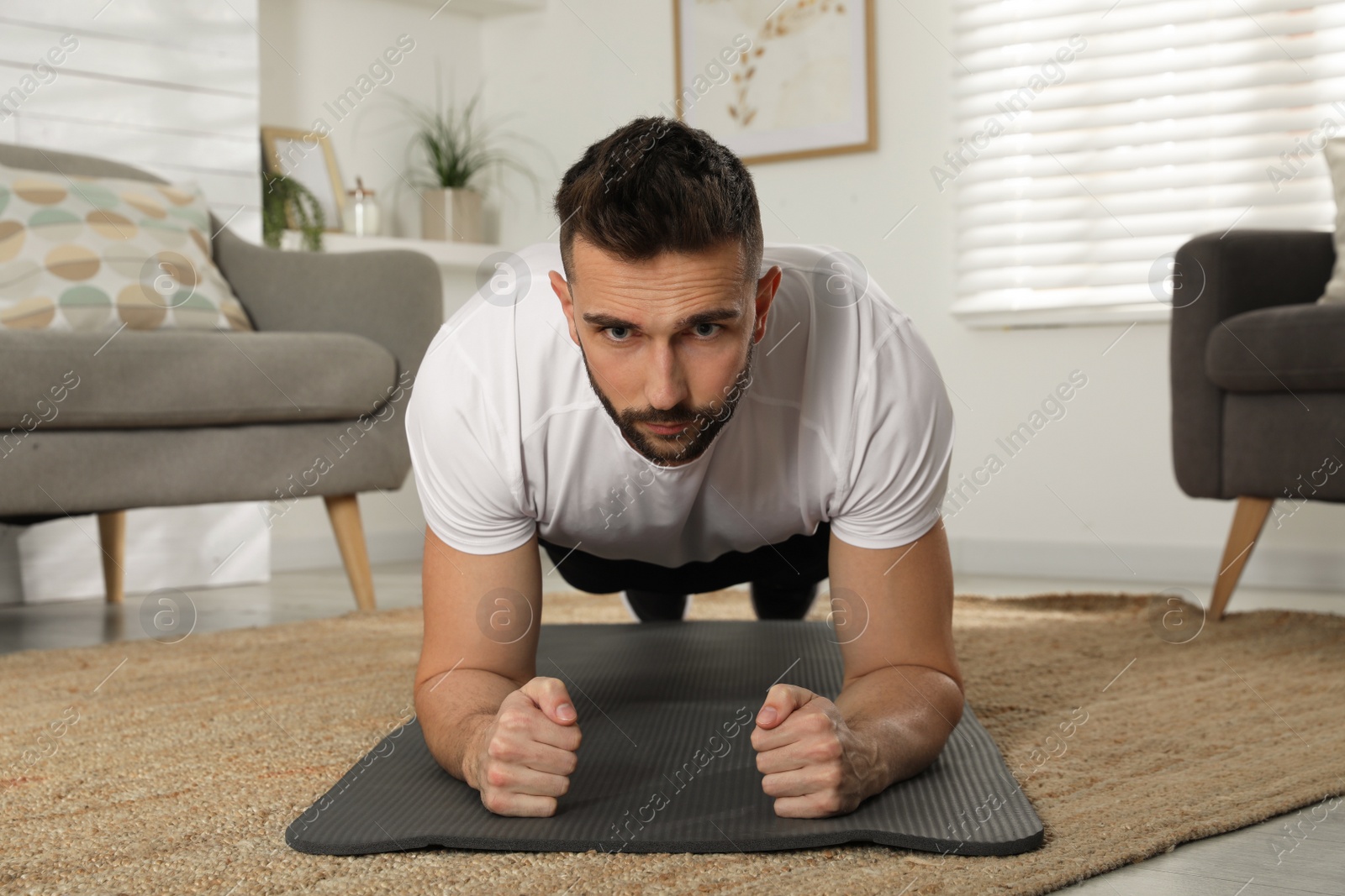 Photo of Handsome man doing plank exercise on yoga mat at home