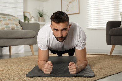 Photo of Handsome man doing plank exercise on yoga mat at home