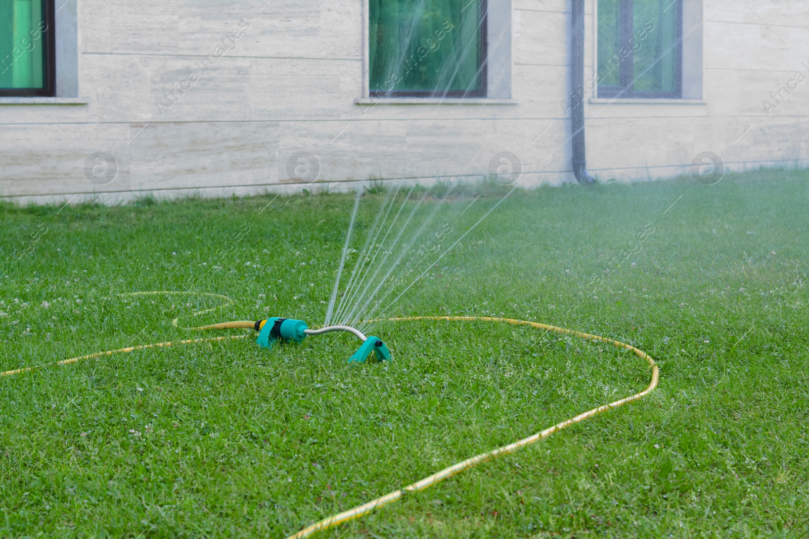 Photo of Automatic sprinkler watering green grass on lawn outdoors