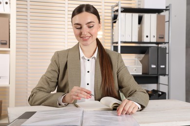 Photo of Happy woman taking notes at light wooden table in office