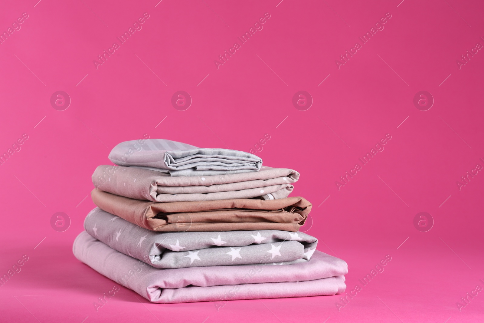 Photo of Stack of clean bed sheets on pink background