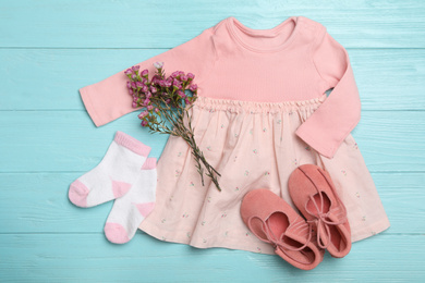 Photo of Flat lay composition with child's clothes and flowers on light blue wooden table