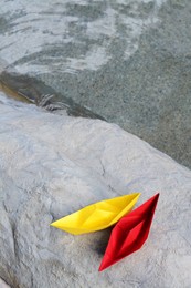 Beautiful yellow and red paper boats on stone near water outdoors, above view