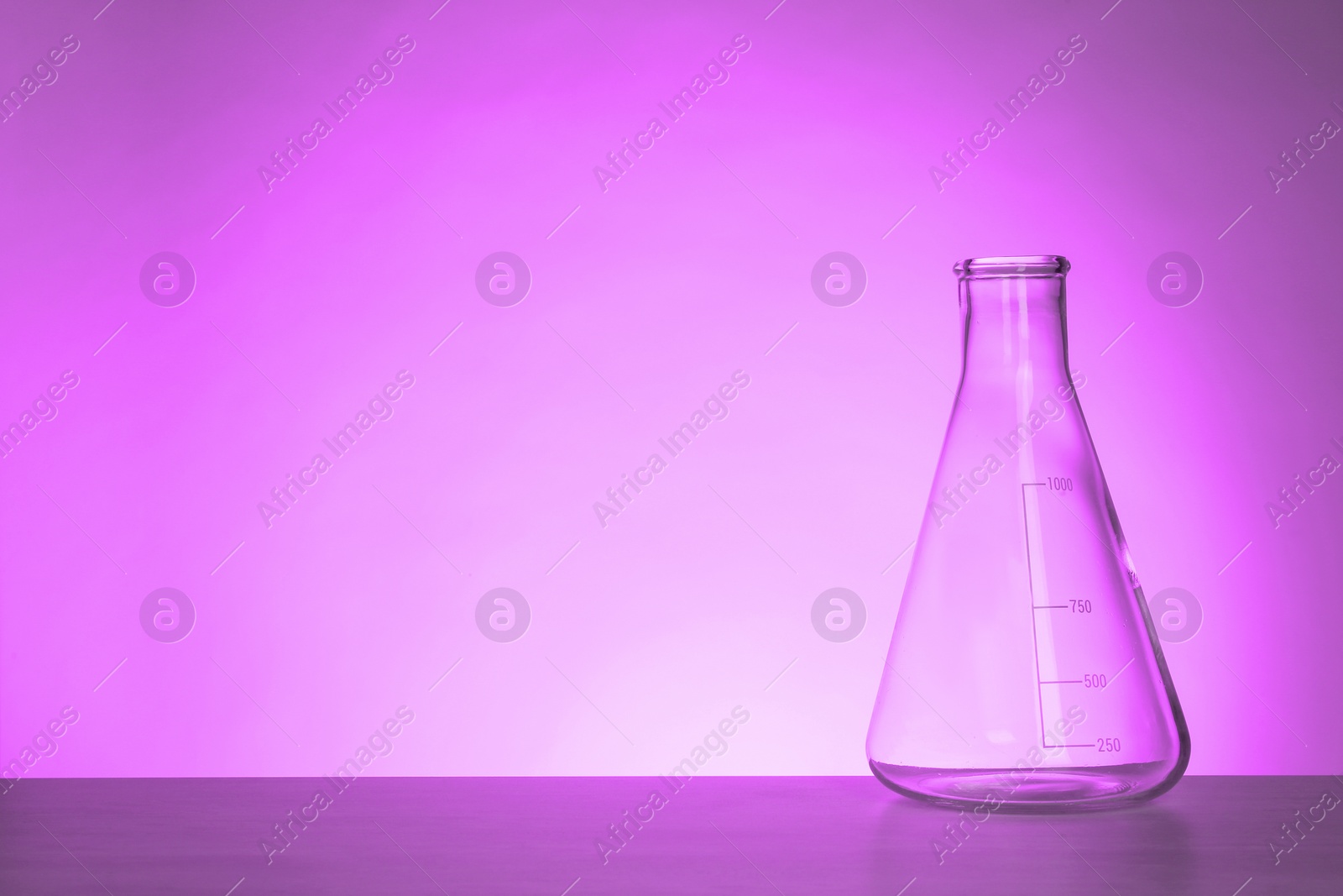 Image of Conical flask with liquid on table, space for text. Toned in violet. Laboratory glassware