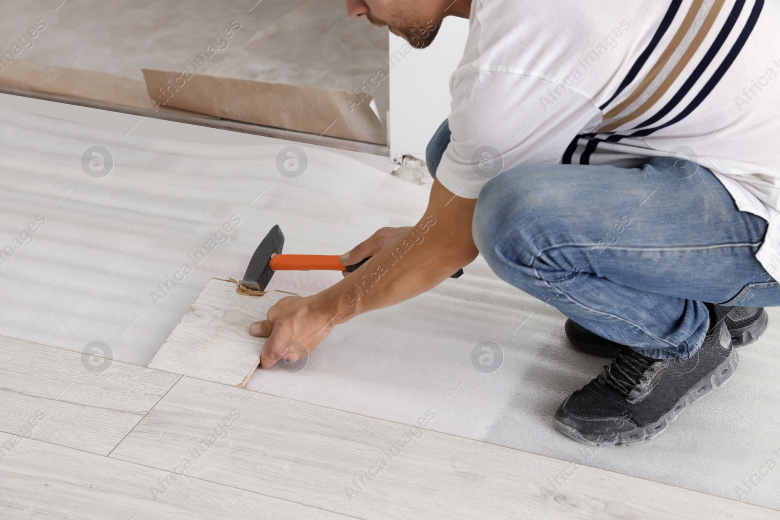 Photo of Man using hammer during installation of new laminate flooring, closeup