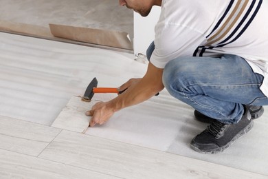 Photo of Man using hammer during installationnew laminate flooring, closeup