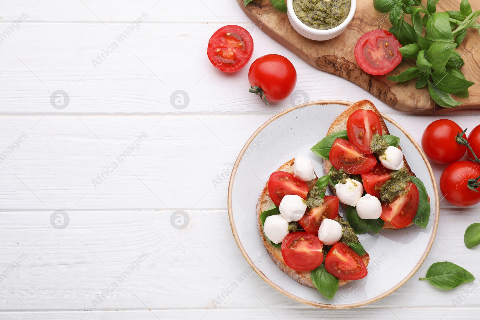 Photo of Delicious Caprese sandwiches with mozzarella, tomatoes, basil and pesto sauce on white wooden table, flat lay. Space for text