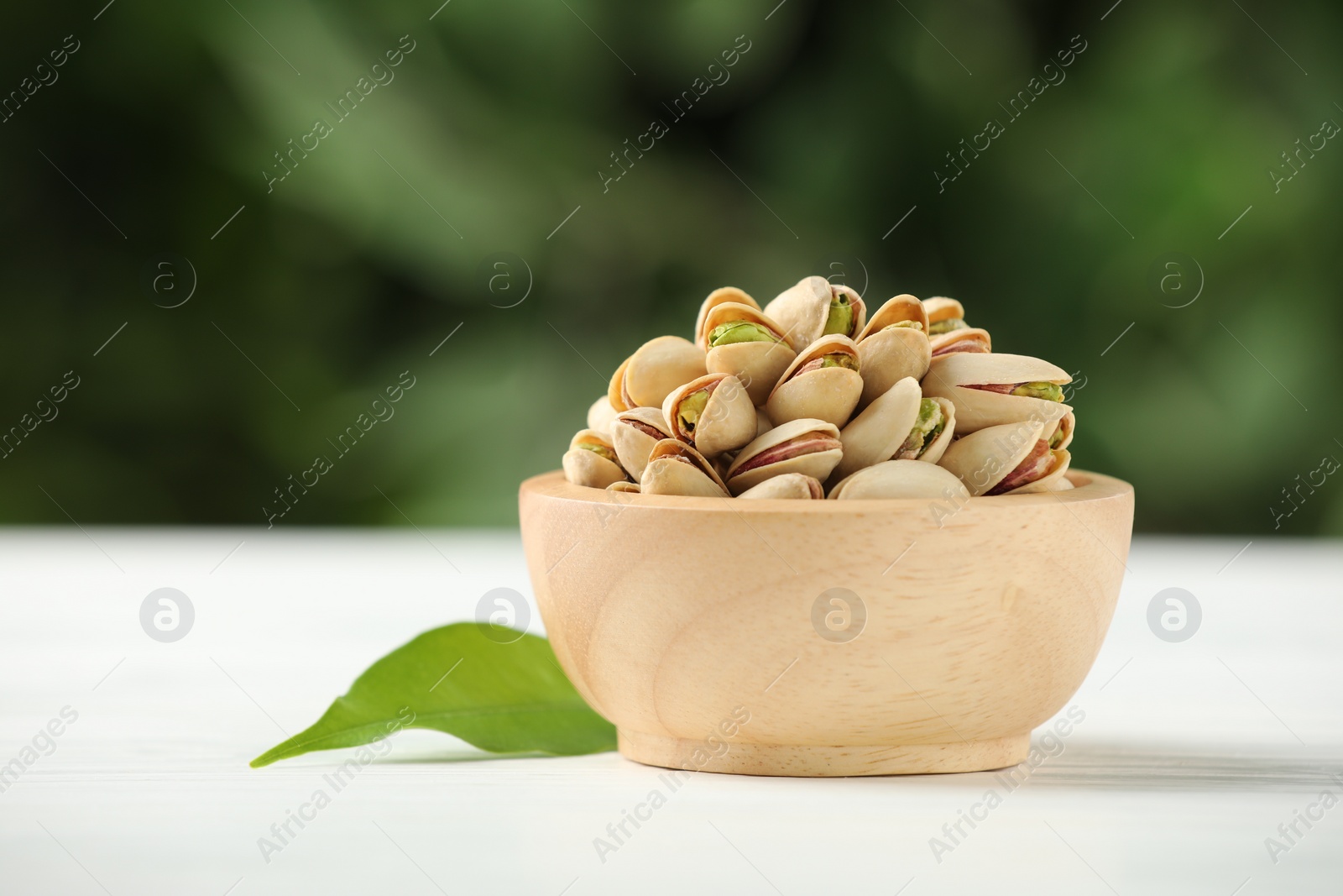 Photo of Tasty pistachios in bowl on white wooden table against blurred background, closeup