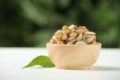 Tasty pistachios in bowl on white wooden table against blurred background, closeup