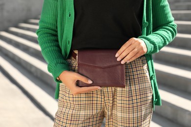 Photo of Young African American woman with stylish waist bag on stairs outdoors, closeup