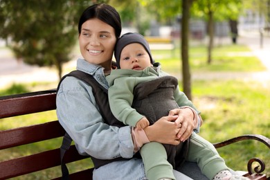 Photo of Mother holding her child in sling (baby carrier) on bench in park