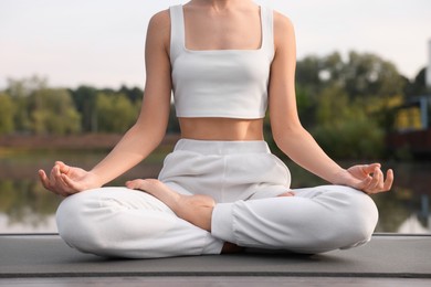Photo of Woman practicing Padmasana on yoga mat outdoors, closeup. Lotus pose