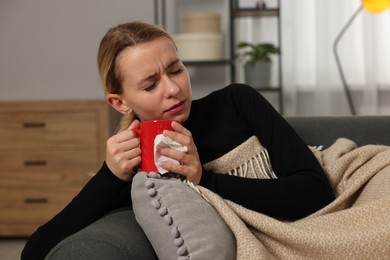 Photo of Sick woman with tissue and cup of drink on sofa at home. Cold symptoms