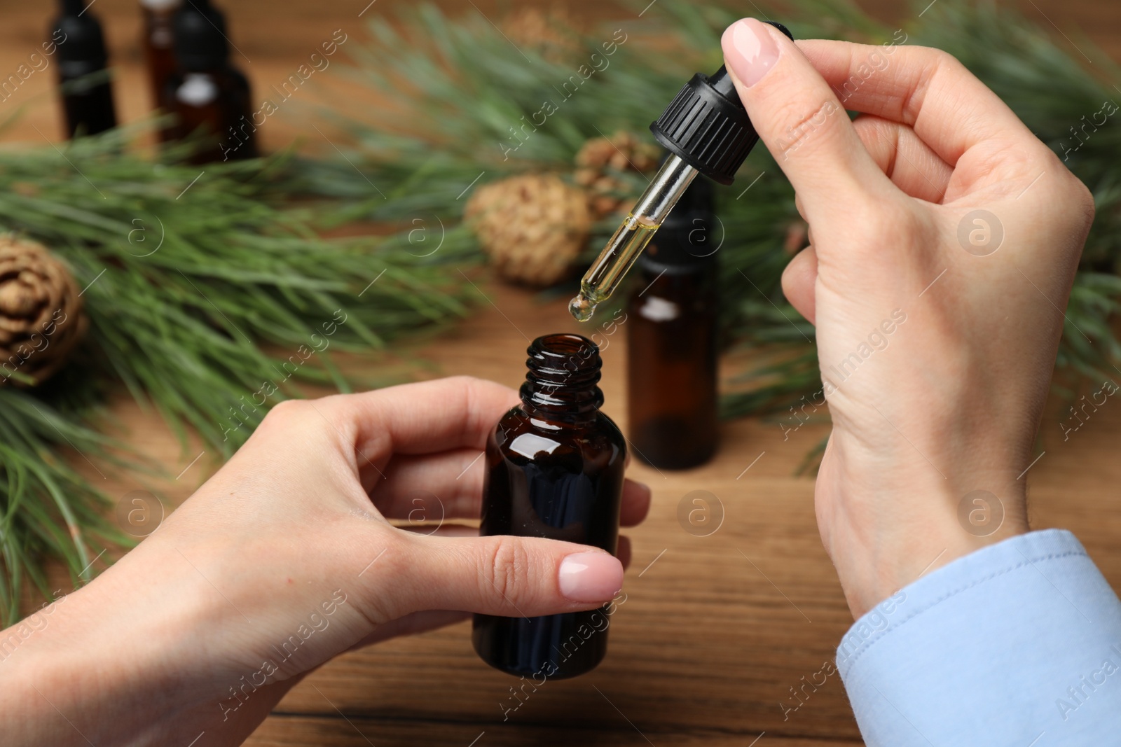 Photo of Woman holding pipette with pine essential oil over bottle at wooden table, closeup