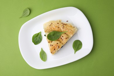 Photo of Piece of delicious puff pastry with spinach on green background, top view