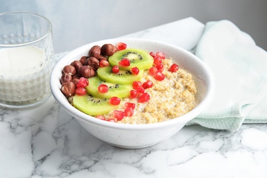 Photo of Bowl of quinoa porridge with hazelnuts, kiwi and pomegranate seeds on marble table