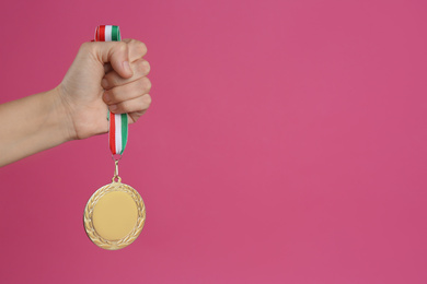 Woman holding golden medal on pink background, closeup. Space for design