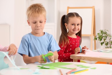 Photo of Cute little children cutting color paper with scissors at desk in kindergarten. Playtime activities