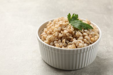 Photo of Tasty pearl barley porridge in bowl on light textured table, closeup. Space for text