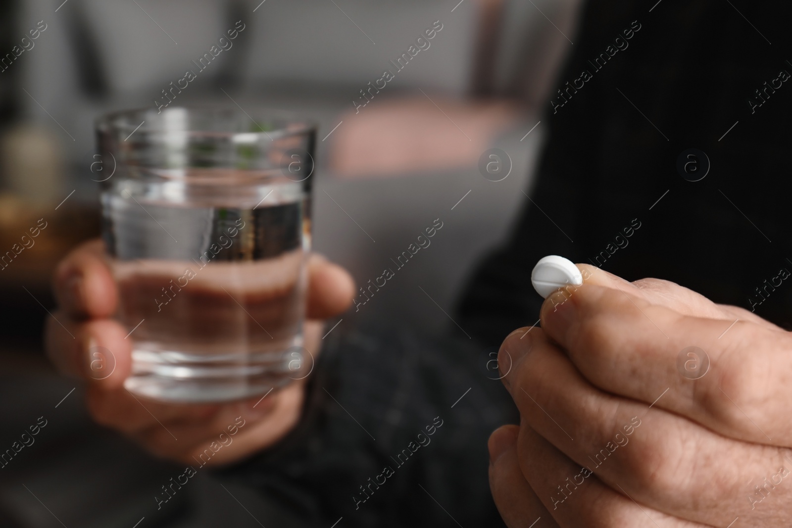 Photo of Senior man holding pill and glass of water indoors, closeup