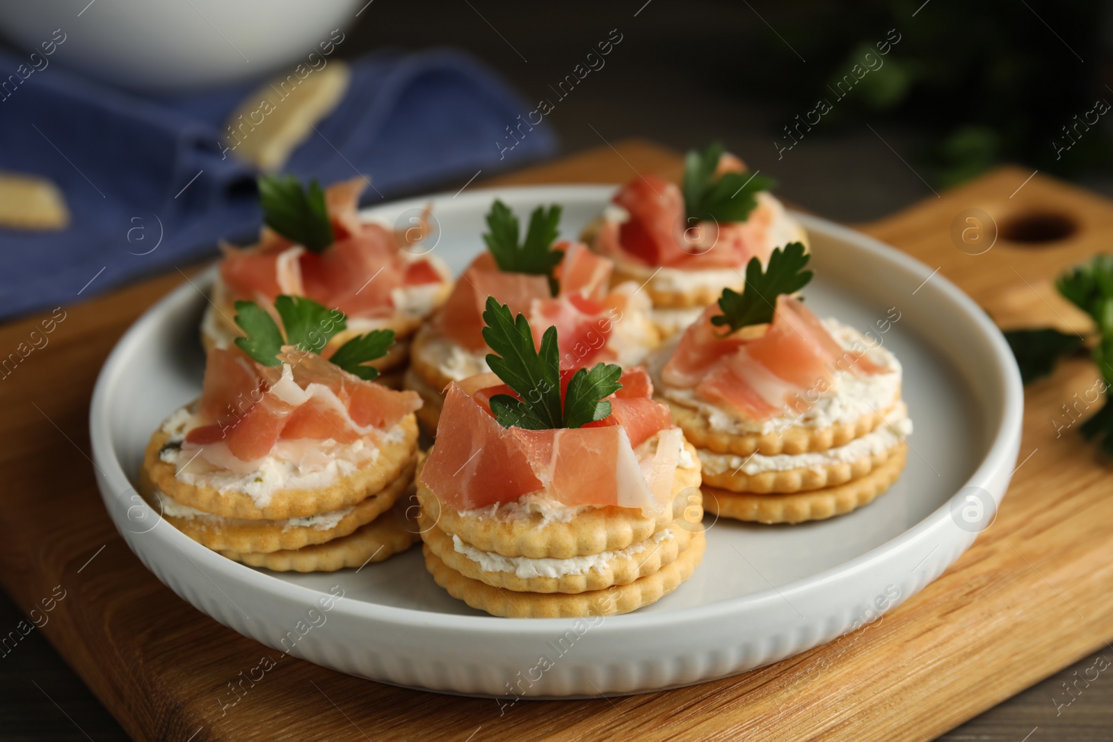 Photo of Delicious crackers with cream cheese, prosciutto and parsley on table