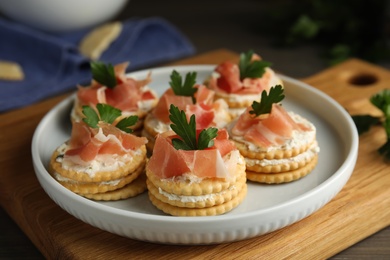 Photo of Delicious crackers with cream cheese, prosciutto and parsley on table