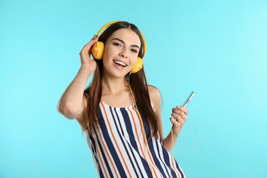 Beautiful young woman listening to music with headphones on color background