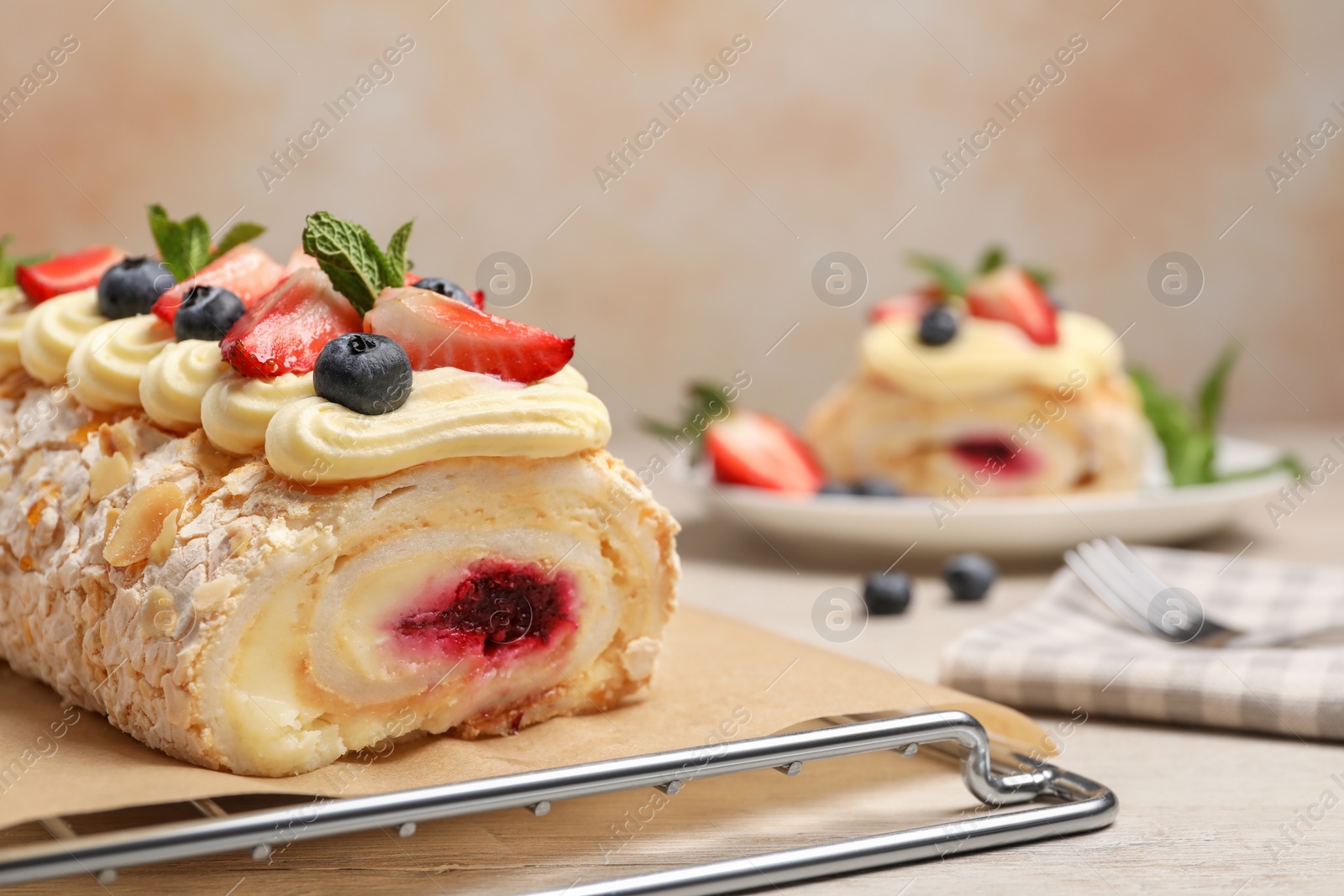 Photo of Tasty meringue roll with jam, cream, strawberry, blueberry and mint on white wooden table, closeup. Space for text
