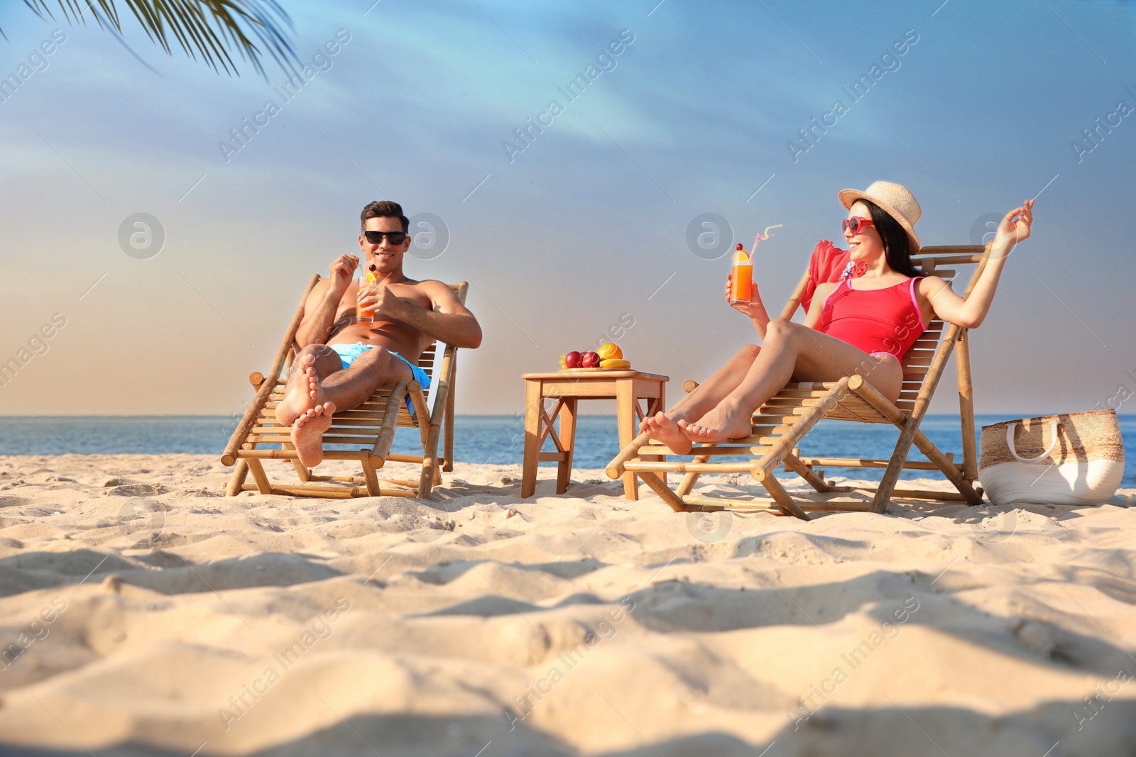 Photo of Couple with drinks resting on sunny beach at resort