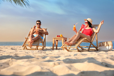 Photo of Couple with drinks resting on sunny beach at resort