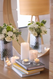 Photo of Beautiful burning candles, books and flowers on table at home