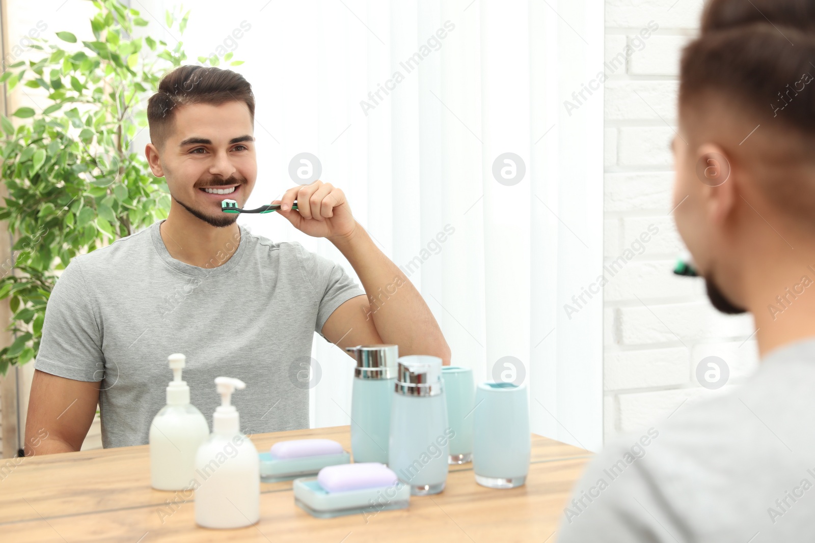 Photo of Young man brushing teeth near mirror in bathroom at home