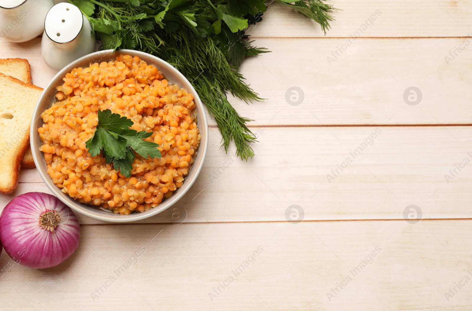 Photo of Delicious red lentils with parsley in bowl served on wooden table, flat lay. Space for text