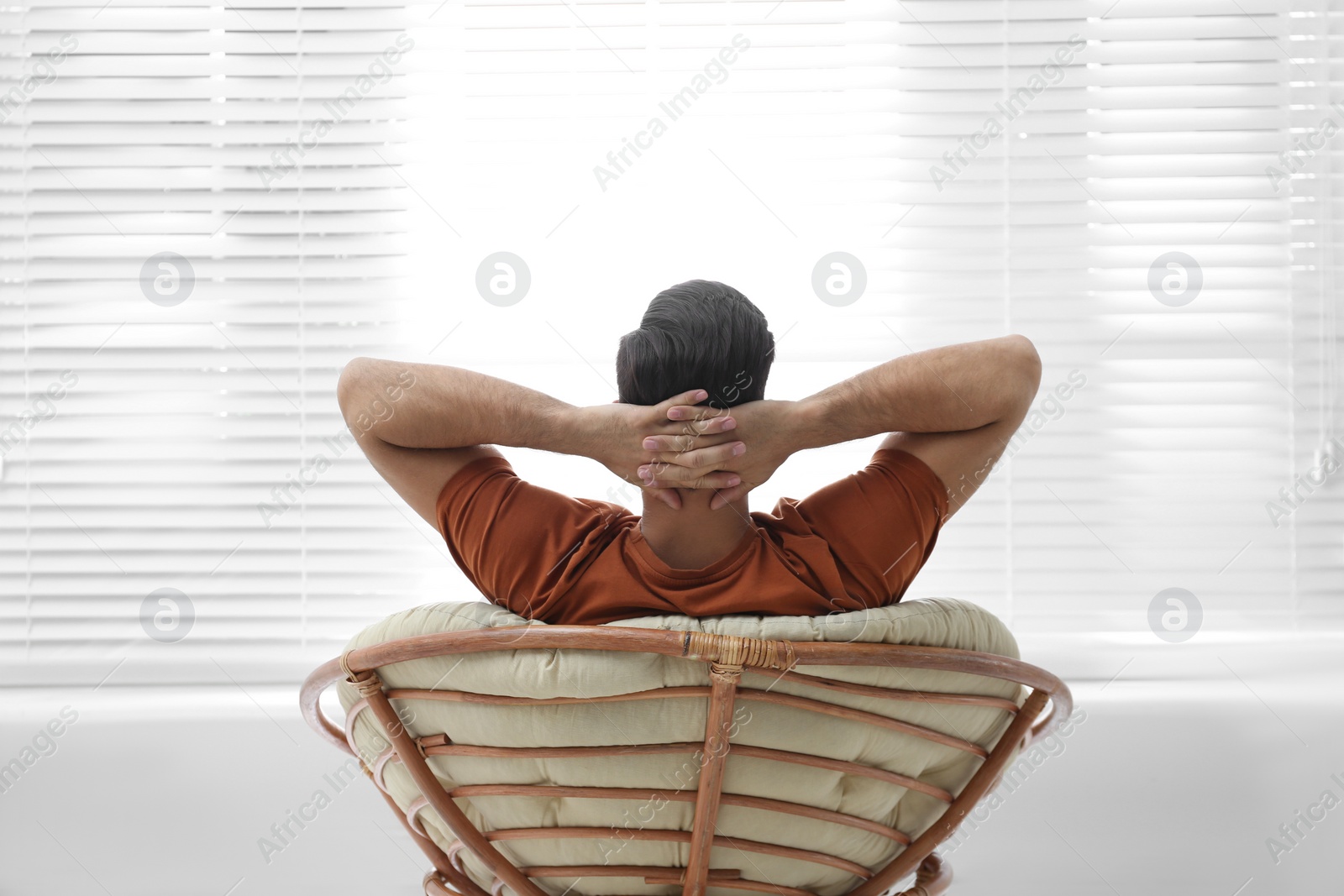 Photo of Man relaxing in papasan chair near window at home, back view