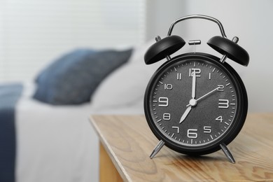 Black alarm clock on wooden nightstand in bedroom, space for text