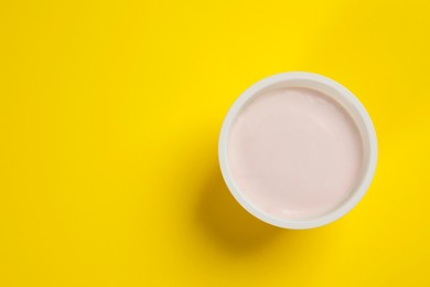 Photo of Plastic cup with tasty yogurt on yellow background, top view. Space for text