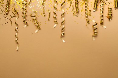 Photo of Shiny golden serpentine streamers and confetti on beige background, flat lay. Space for text