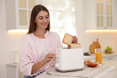 Photo of Young woman using toaster at table in kitchen