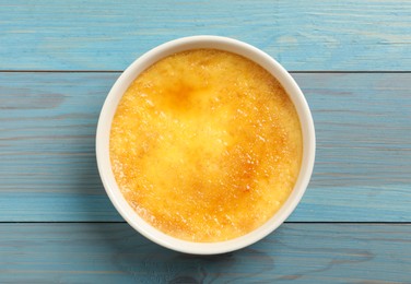 Photo of Delicious creme brulee in ceramic ramekin on light blue wooden table, top view