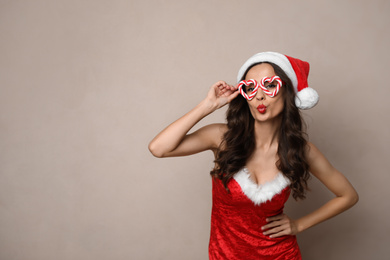 Funny woman in Christmas costume with party glasses on beige background, space for text