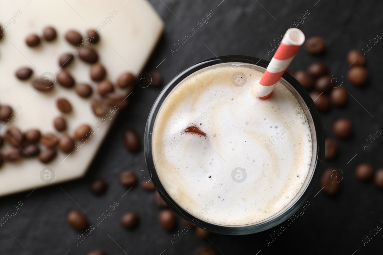 Photo of Refreshing iced coffee with milk in glass and beans on dark gray table, top view