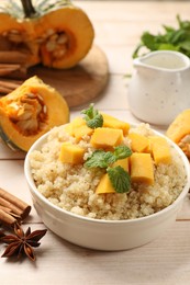 Tasty quinoa porridge with pumpkin, mint in bowl and spices on light wooden table