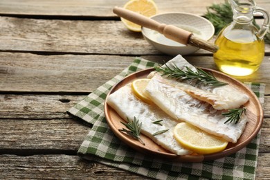 Photo of Fresh raw cod fillets with rosemary and lemon on wooden table. Space for text
