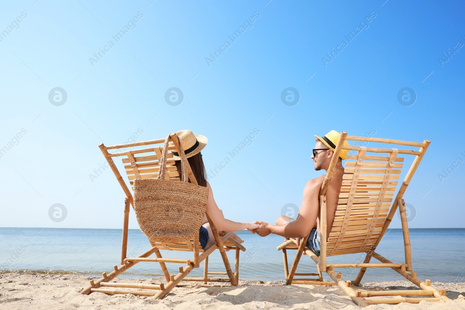 Photo of Young couple relaxing in deck chairs on beach