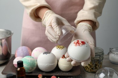 Photo of Woman in gloves with self made bath bomb at table, closeup